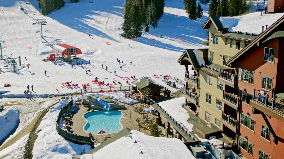A vibrant scene showing active skiers on the slopes, the resort’s pool area, and the resort building framed by winter scenery. The image balances dynamic action on the slopes with the tranquil poolside, showcasing the duality of excitement and relaxation available at the resort.