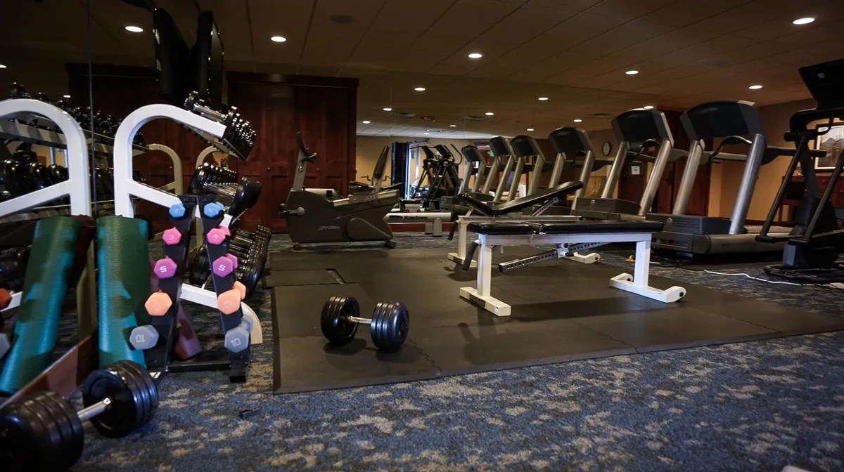 A modern fitness center equipped with dumbbells, various exercise machines, and a weight bench. The bright, open space encourages guests to pursue wellness during their stay.