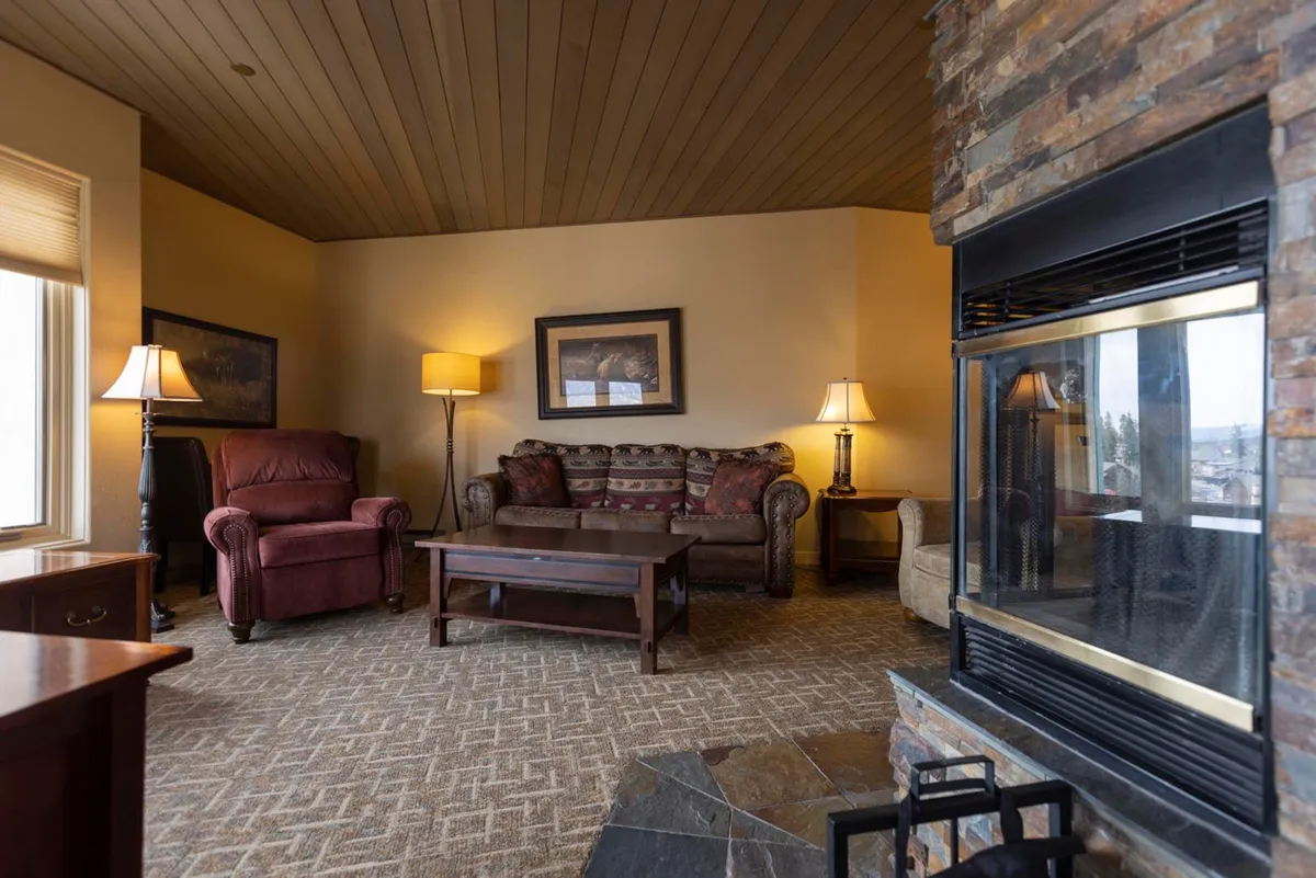 A warm, intimate seating arrangement centers on a crackling fireplace, with plush chairs and a coffee table creating a perfect nook for conversation, reading, or unwinding. Gentle lighting from lamps adds a welcoming ambiance, ideal for intimate evenings after a day on the slopes.