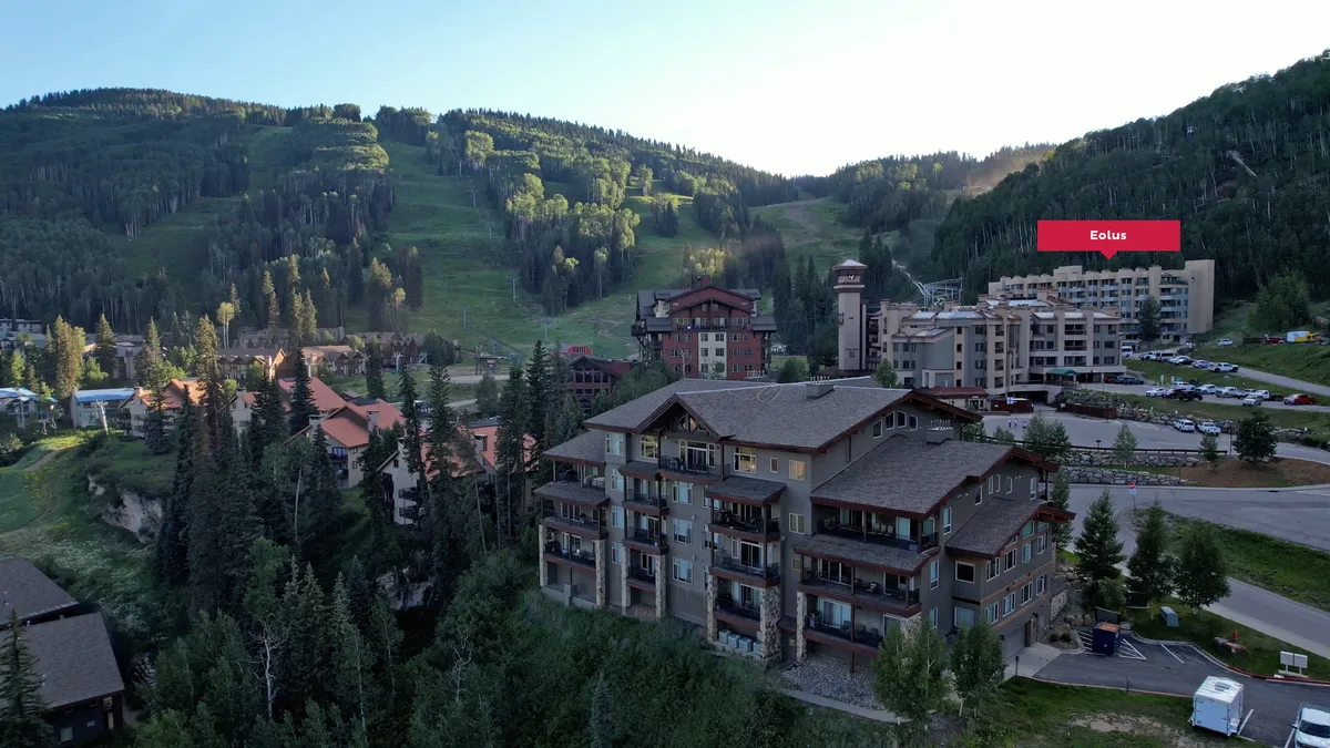 A tranquil exterior shot featuring lush greenery, residential resort buildings, and a panoramic mountain landscape under a vibrant sky. The scene evokes peacefulness and relaxation, setting the stage for scenic hikes, mountain biking, and outdoor gatherings.