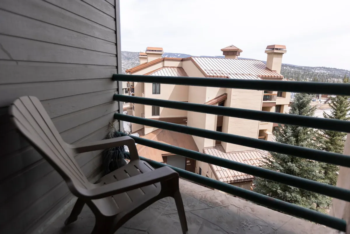 A private deck with a plastic chair and railing overlooking neighboring buildings, offering a tranquil spot to relax and take in the fresh mountain air. The scene suggests a peaceful place for morning coffee or evening stargazing.