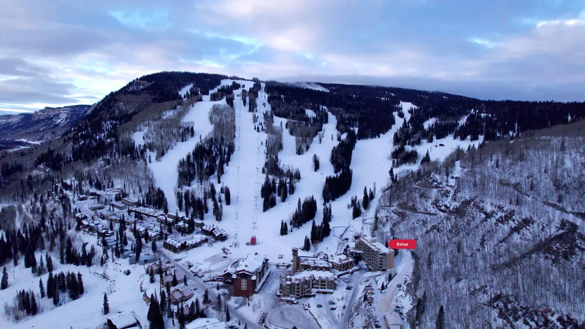 This exterior image showcases snow-covered slopes, ski lifts, resort buildings, and surrounding pine forests, capturing the winter wonderland atmosphere directly adjacent to the property. The early morning light suggests a fresh day of mountain adventure, with the resort at the center of the action.
